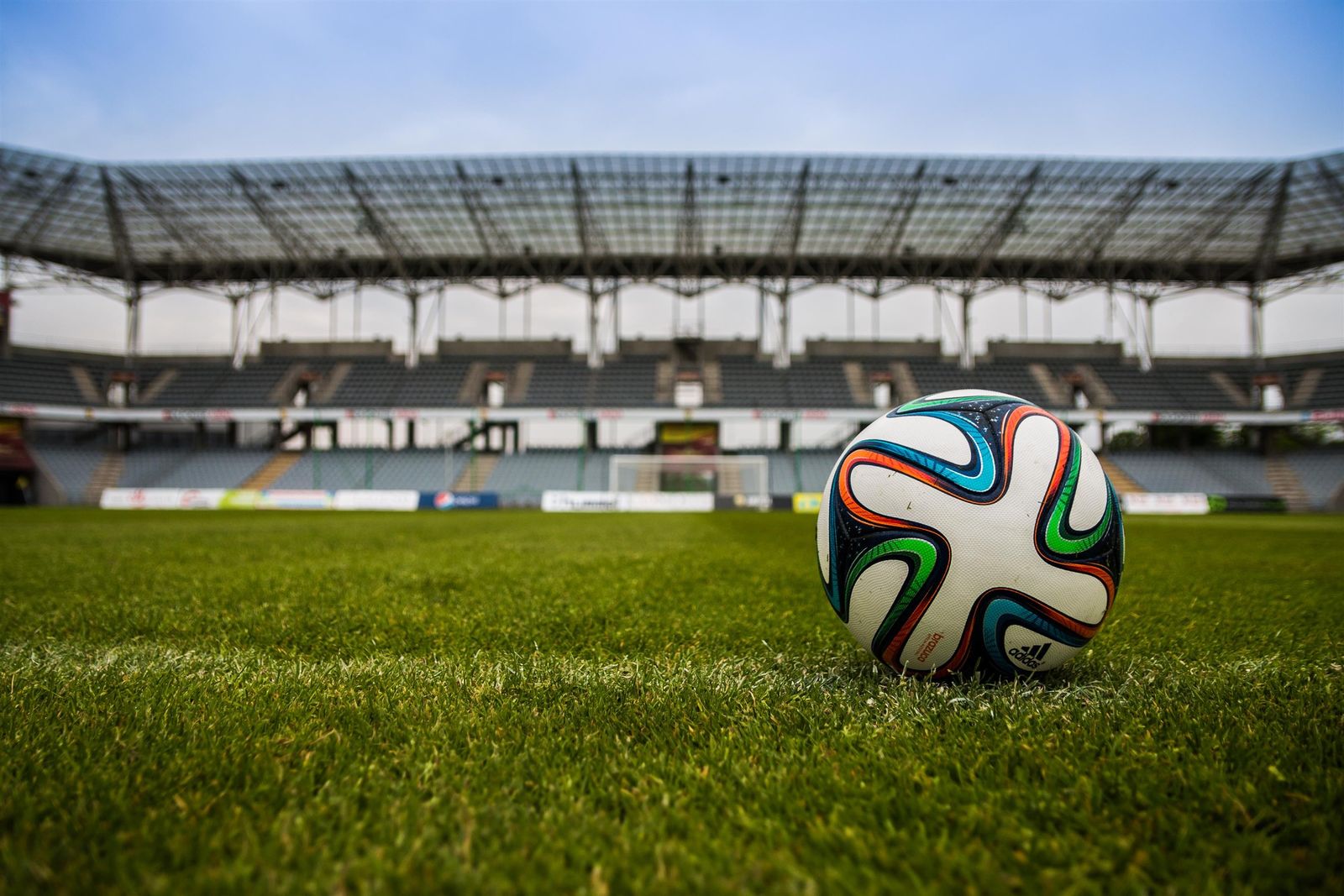 Bola de futebol em campo gramado com arquibancada vazia ao fundo, simbolizando o fim da Copa do Mundo