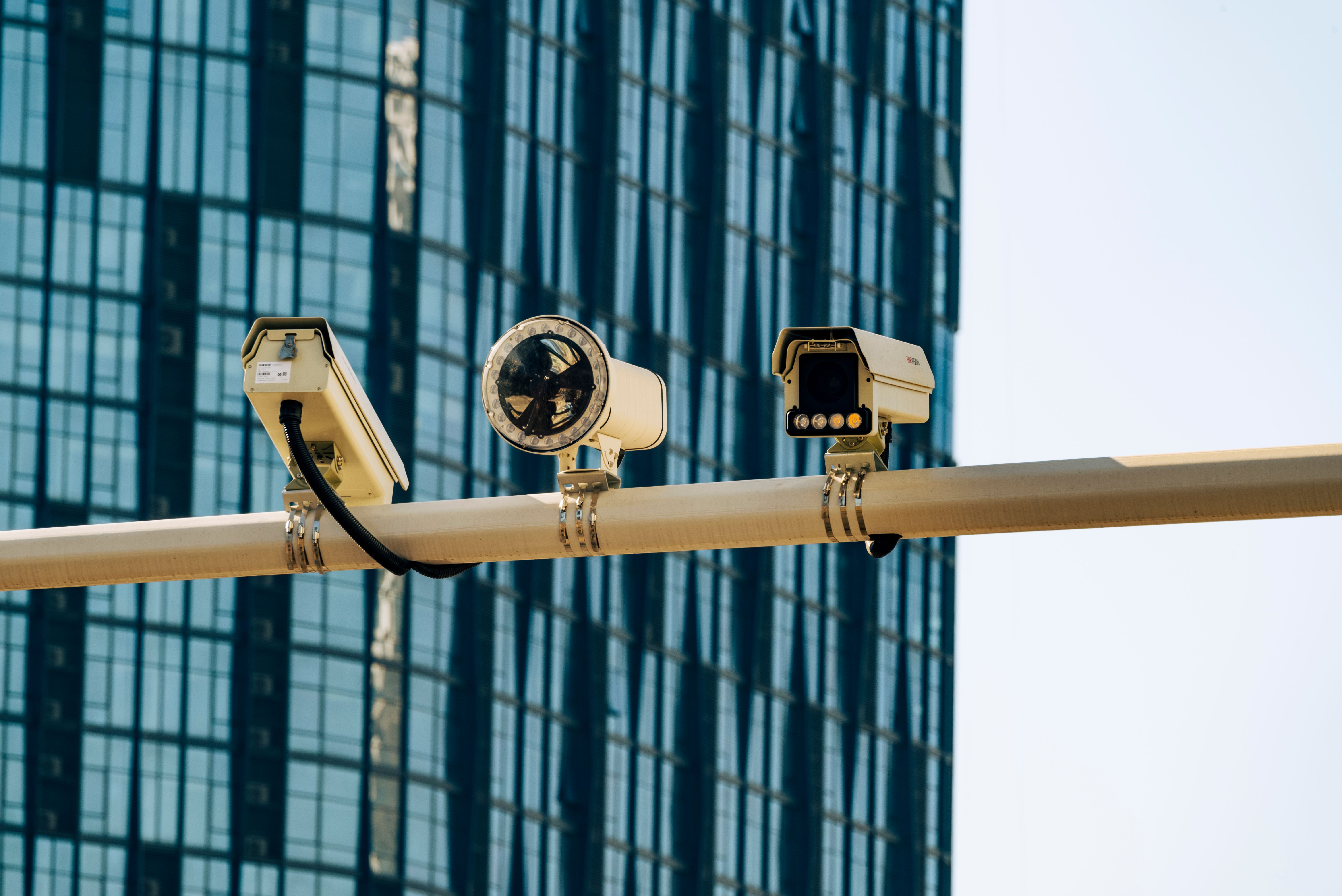 Câmeras de vigilância montadas em poste diante de prédio moderno de vidro, representando sistema de videomonitoramento urbano