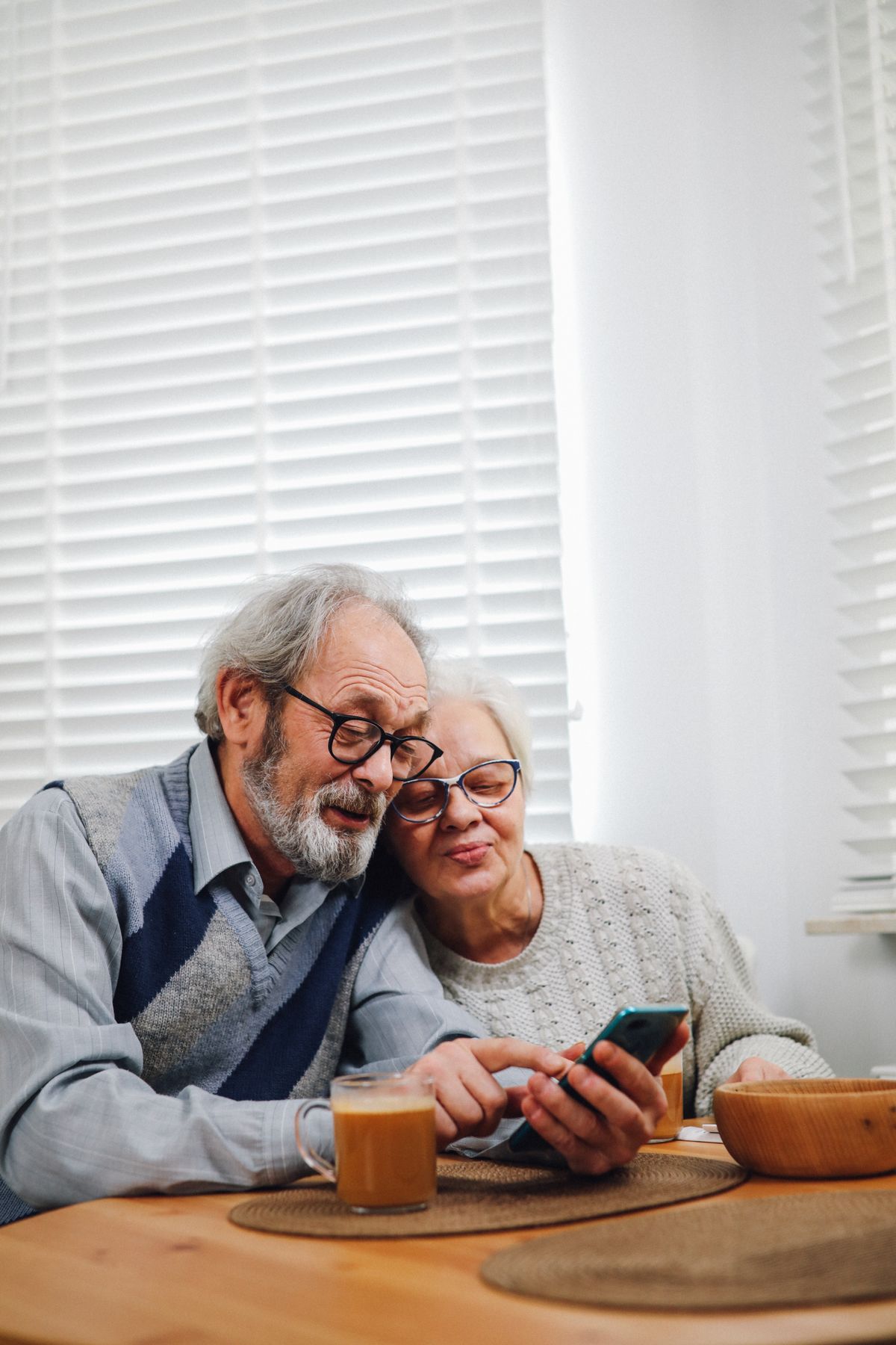 Casal de idosos sorrindo enquanto olha o celular juntos, representando um cliente de plano de saúde popular assinando a adesão pelo WhatsApp