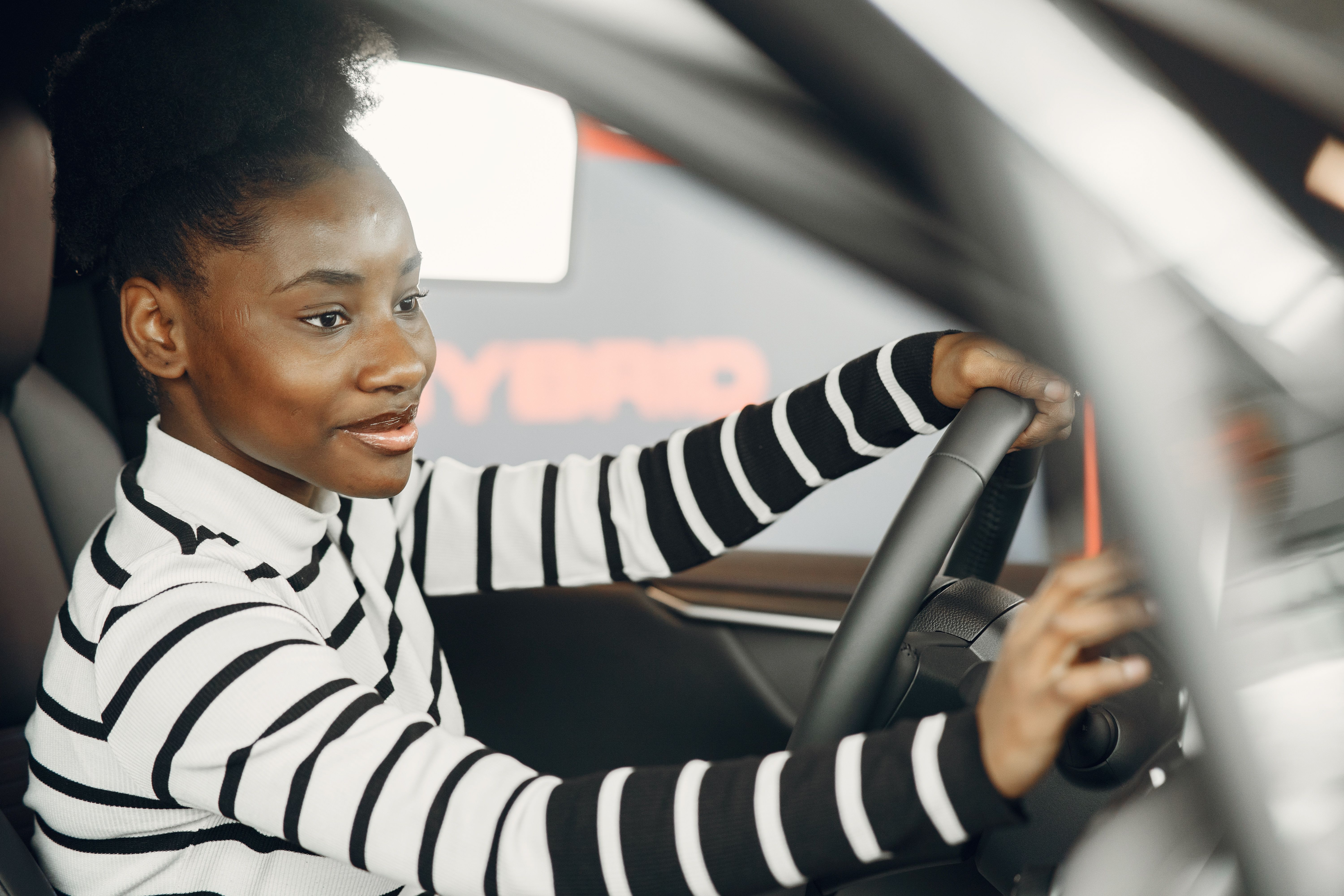 Mulher adulta dirigindo um carro, com as mãos no volante, atenta ao trânsito