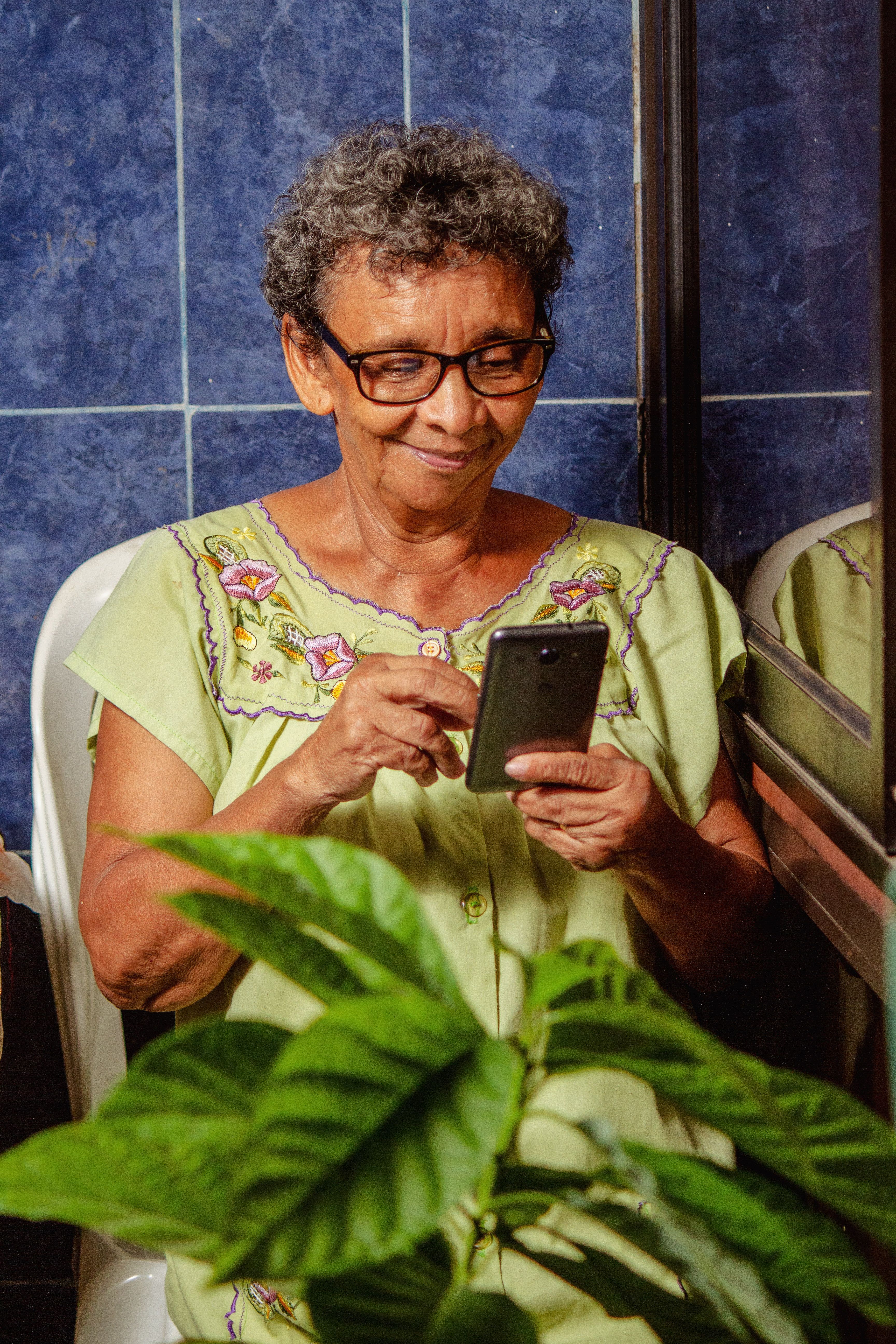 Senhora idosa sorrindo enquanto usa o celular para conversar no WhatsApp