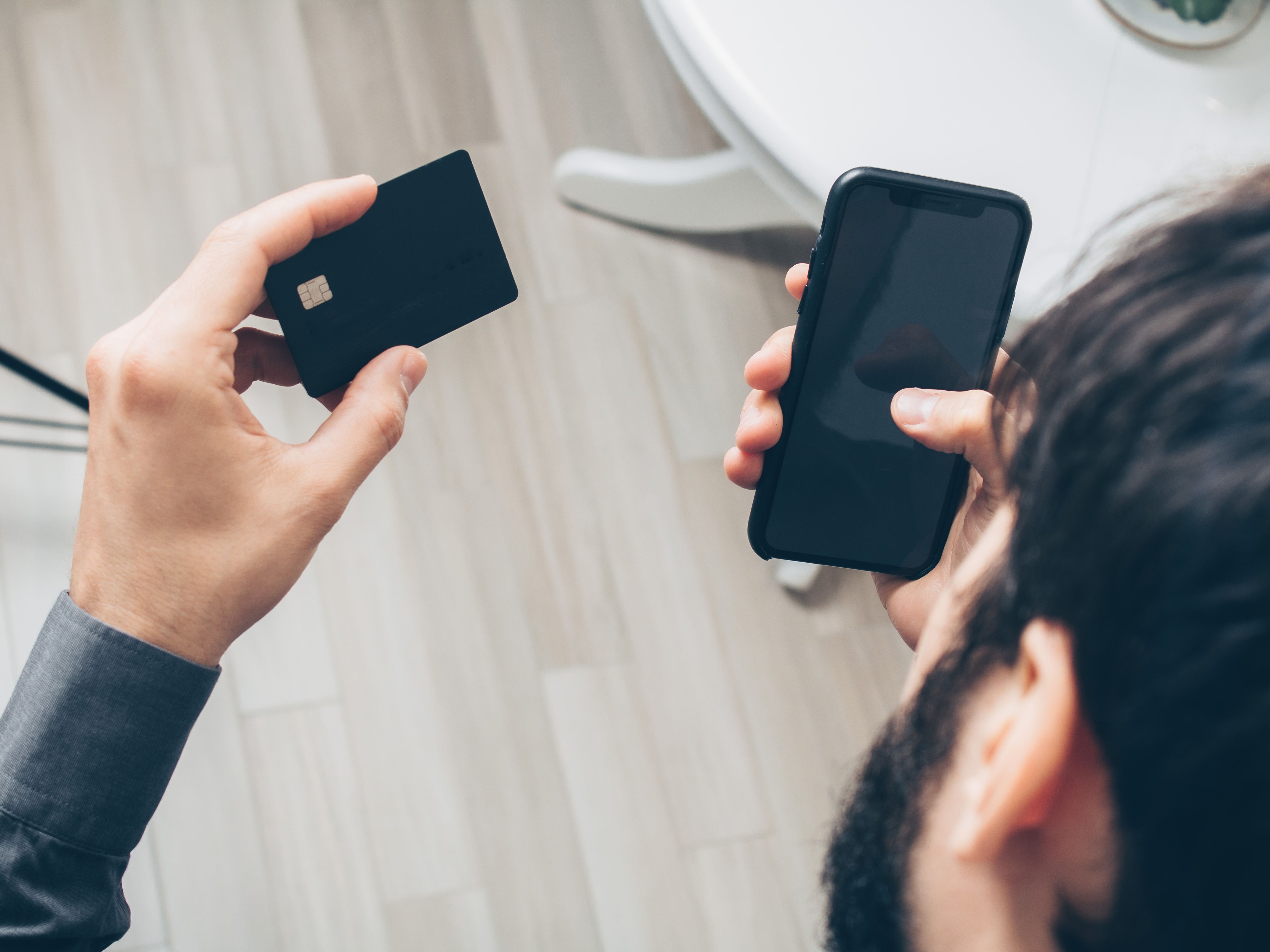 Homem segurando cartão de crédito e olhando para o smartphone, representando contrato de crédito de fintech assinado pelo WhatsApp
