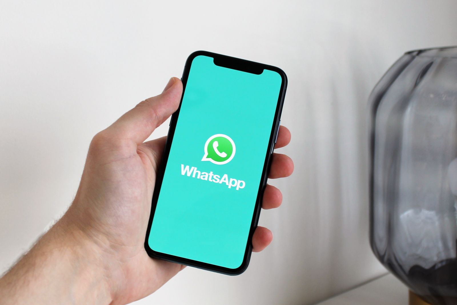 Mão segurando um celular com a tela de abertura do WhatsApp, ilustrando a assinatura de contratos pelo aplicativo