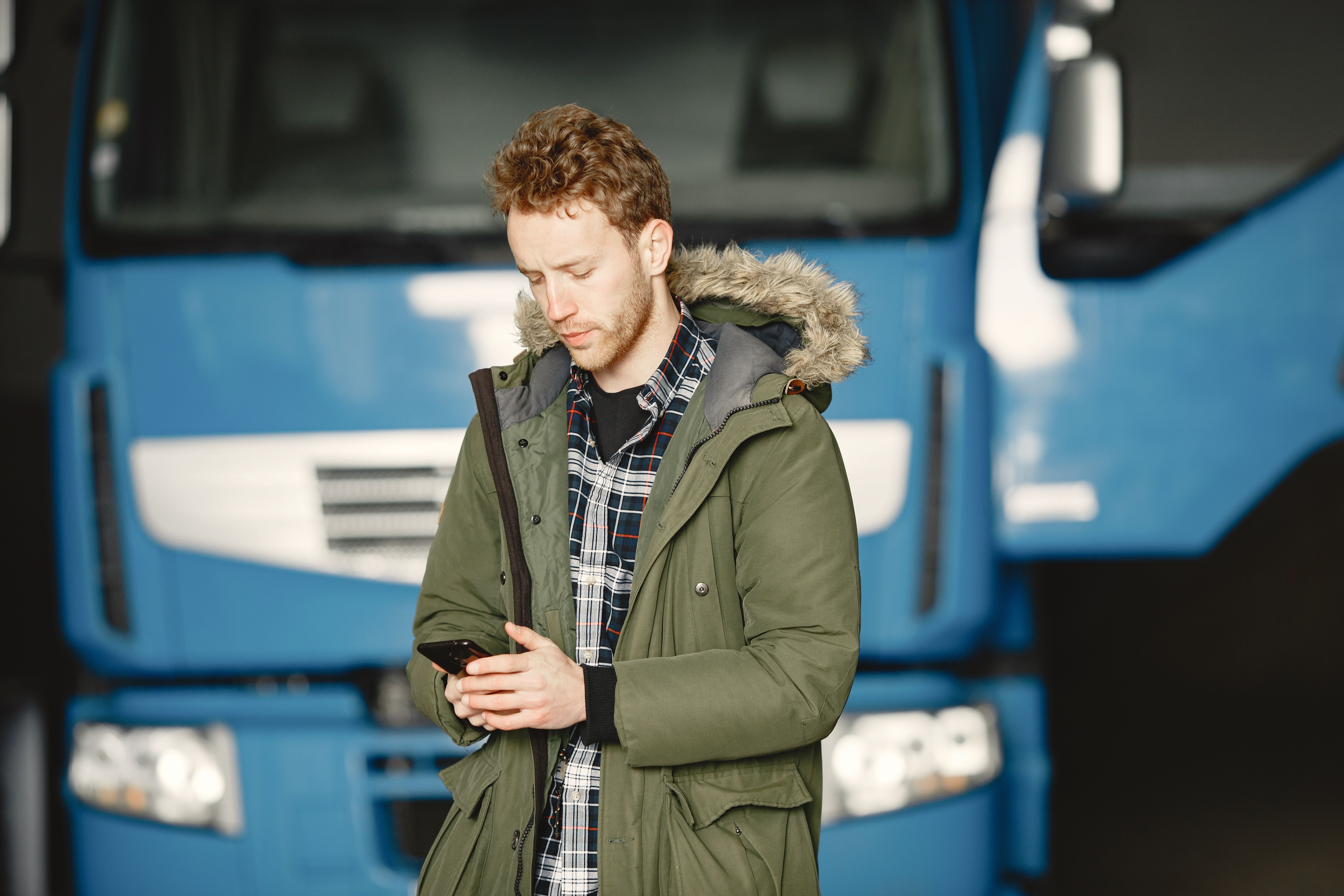 Motorista de caminhão consultando o celular em frente ao veículo, representando a assinatura digital de contrato de frete pelo WhatsApp