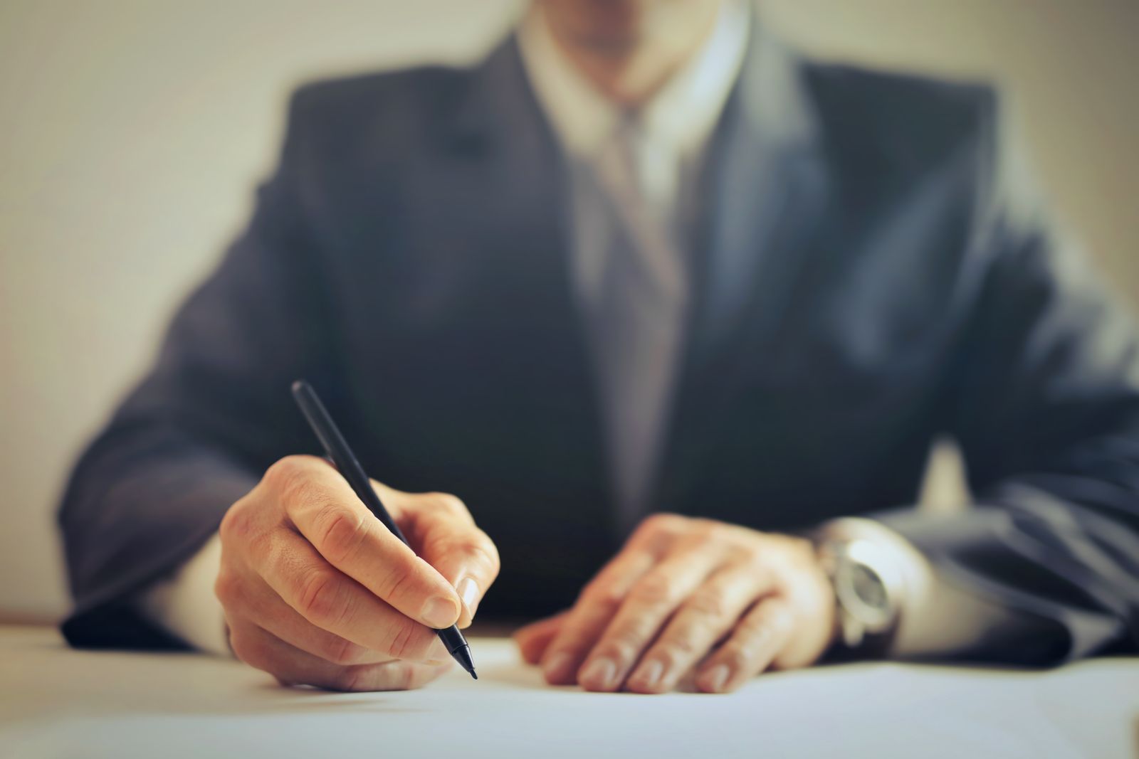 Empresário assinando um contrato com caneta sobre uma mesa, em ambiente de escritório