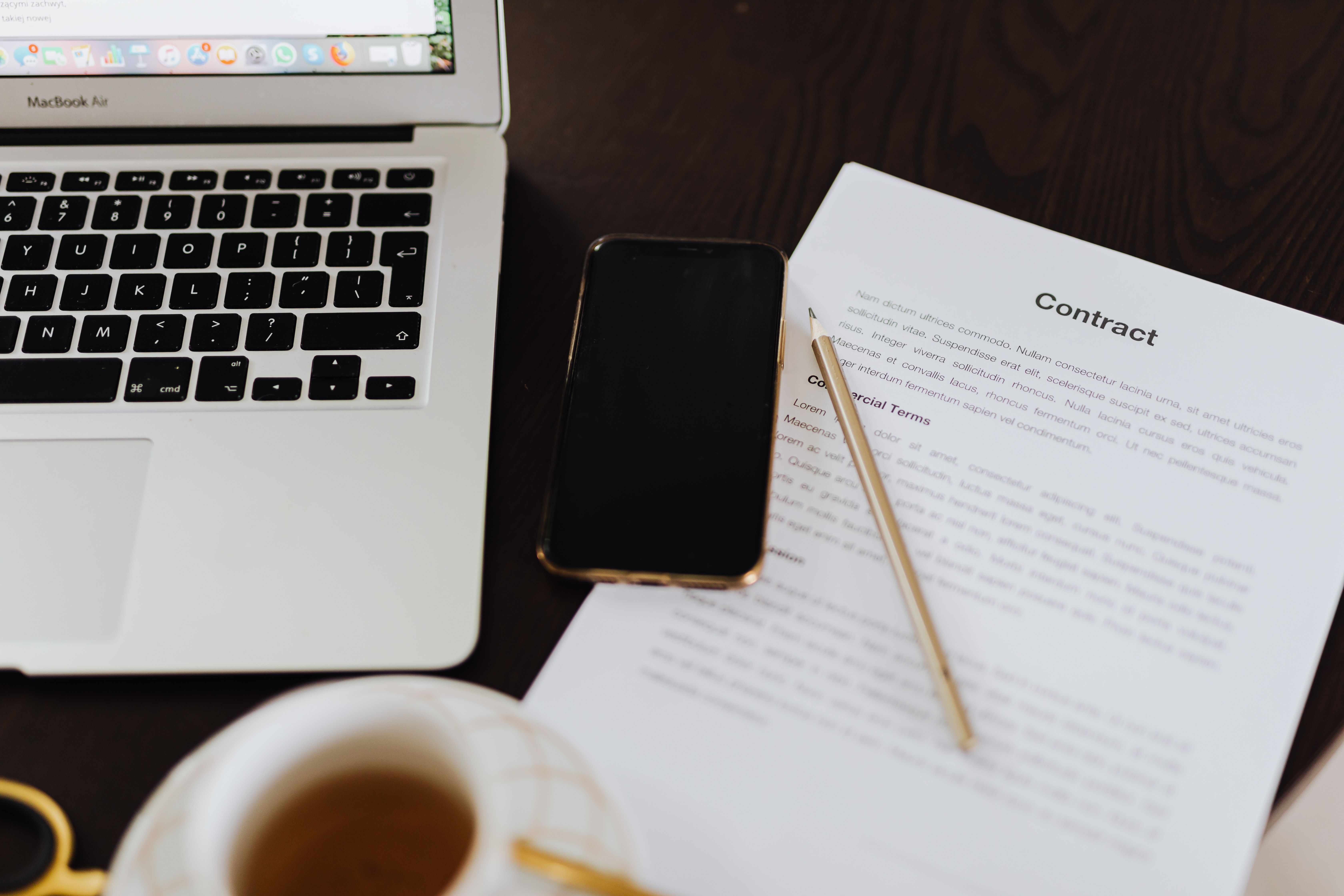 Laptop, celular e um documento de contrato sobre a mesa, representando a assinatura de contrato de uma startup SaaS