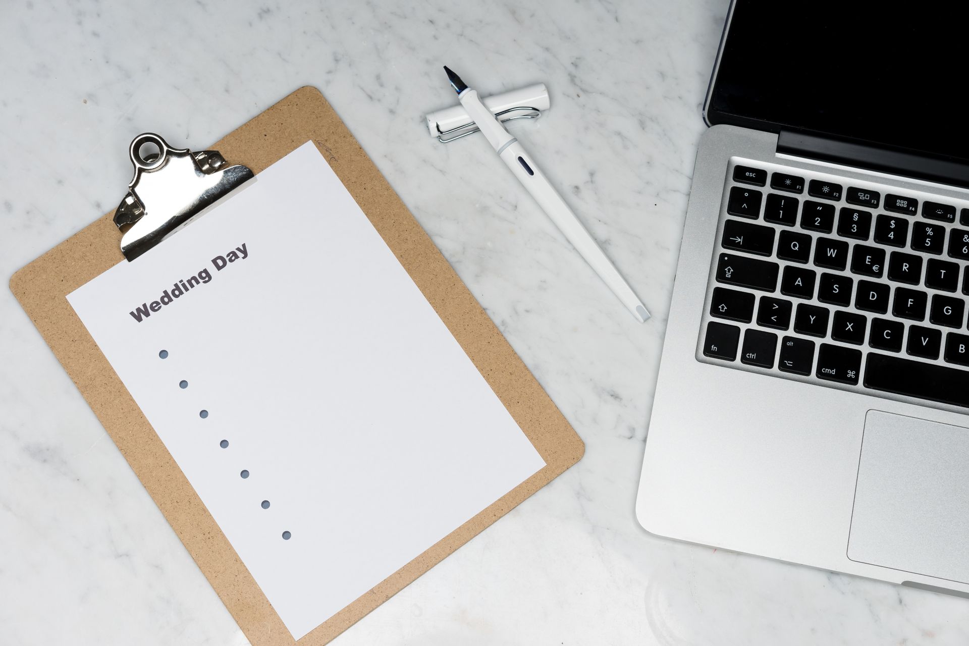 Prancheta com checklist "Wedding Day", caneta e notebook sobre mesa de mármore, representando o planejamento de casamento