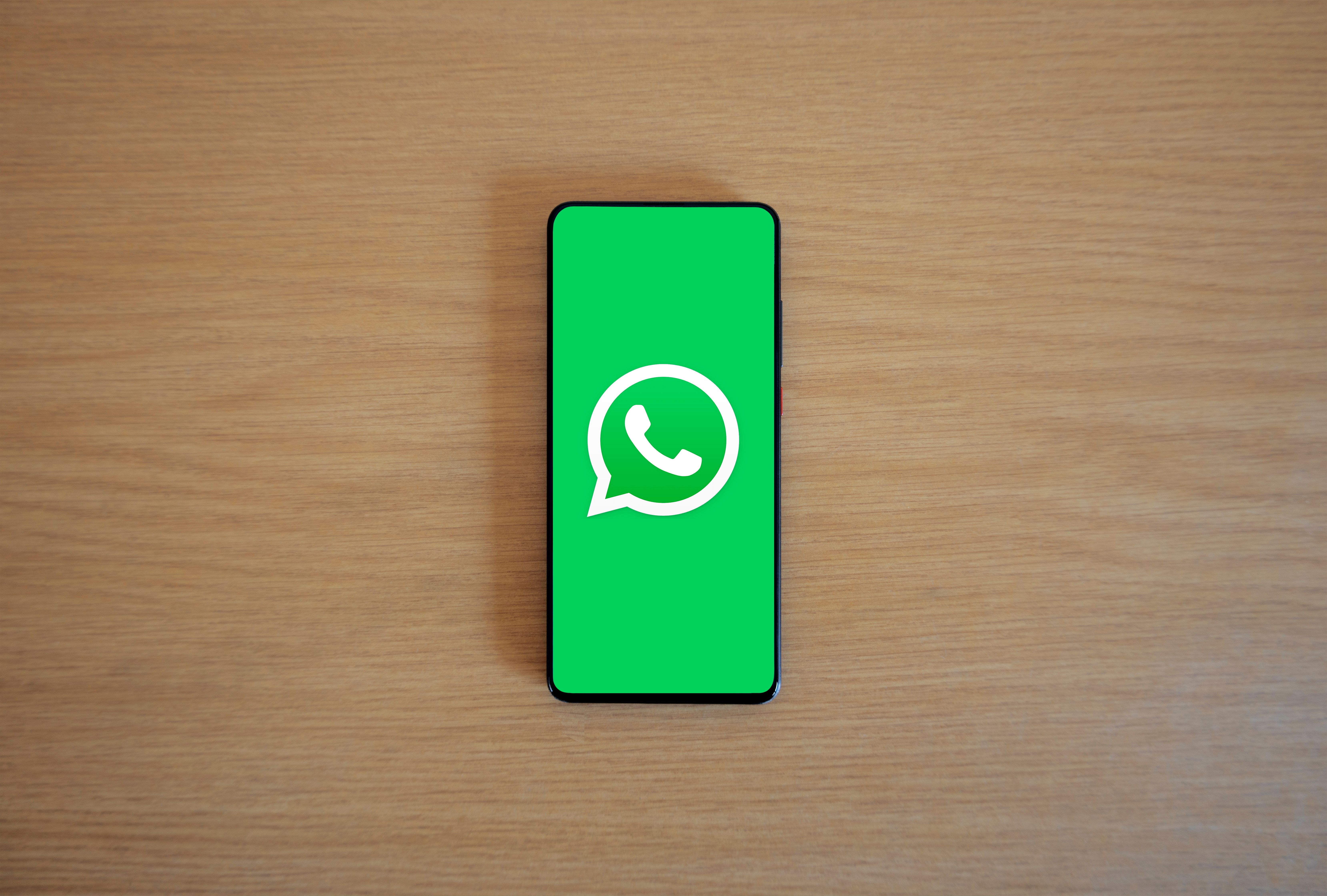 Smartphone sobre mesa de madeira exibindo o logo do WhatsApp em tela cheia